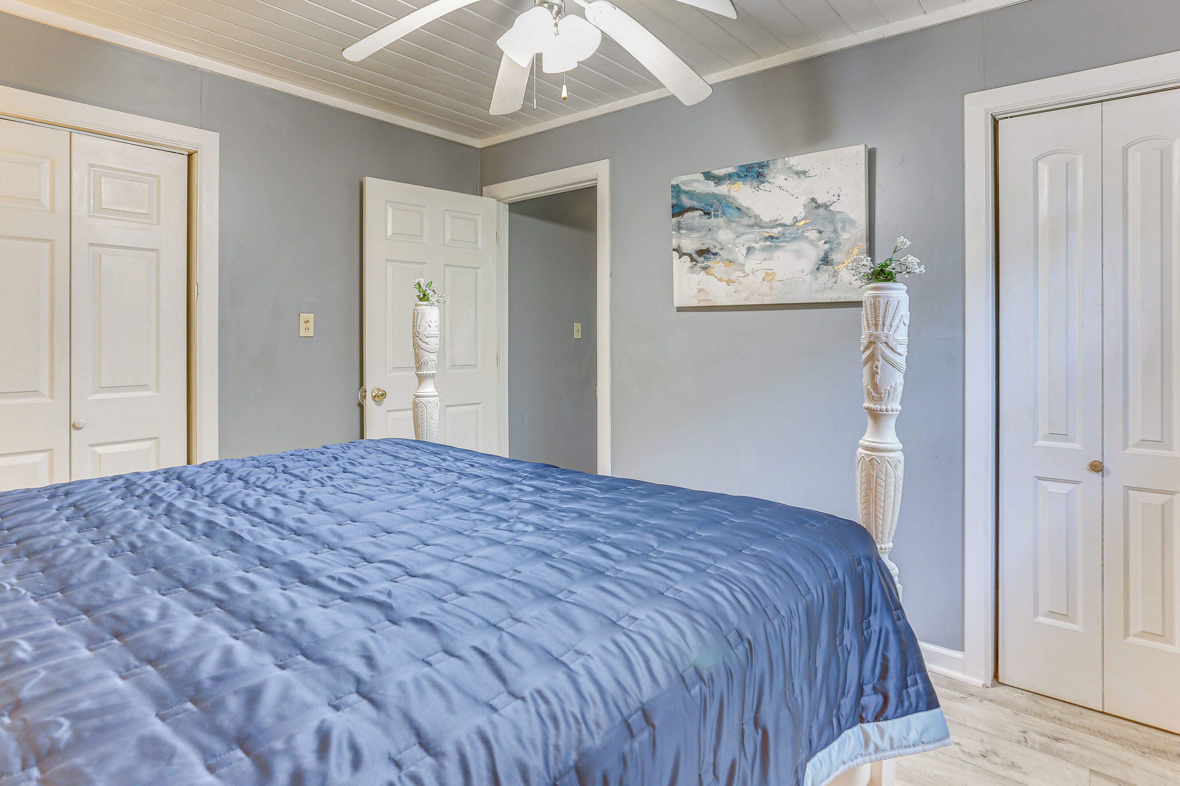 A bedroom with a large bed, a ceiling fan, and a painting on the wall.