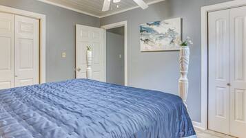 A bedroom with a large bed, a ceiling fan, and a painting on the wall.