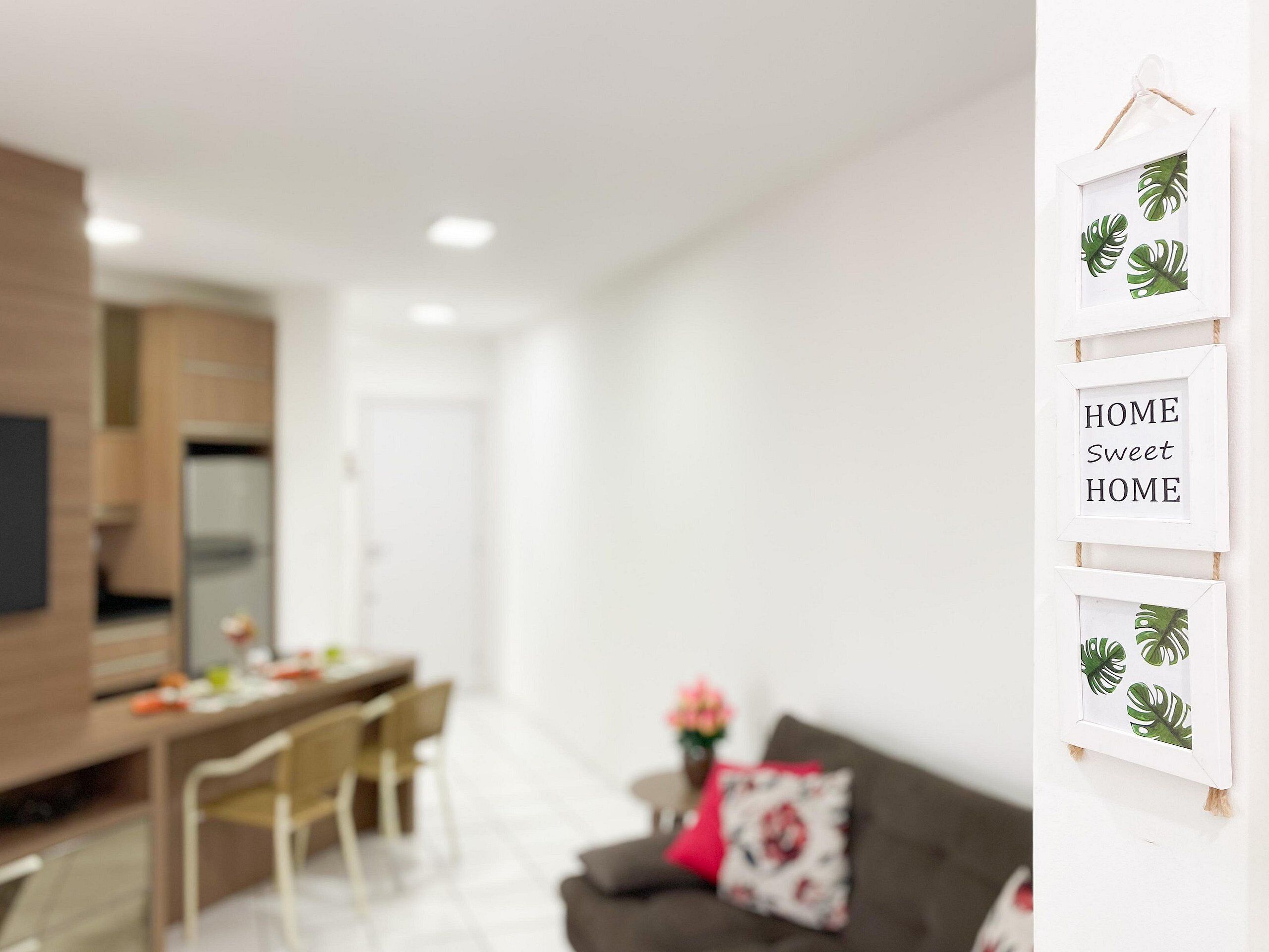 Una sala de estar moderna con comedor, un sofá gris y una almohada roja, y una pared decorada con cuadros.