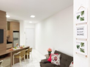 Una sala de estar moderna con comedor, un sofá gris y una almohada roja, y una pared decorada con cuadros.