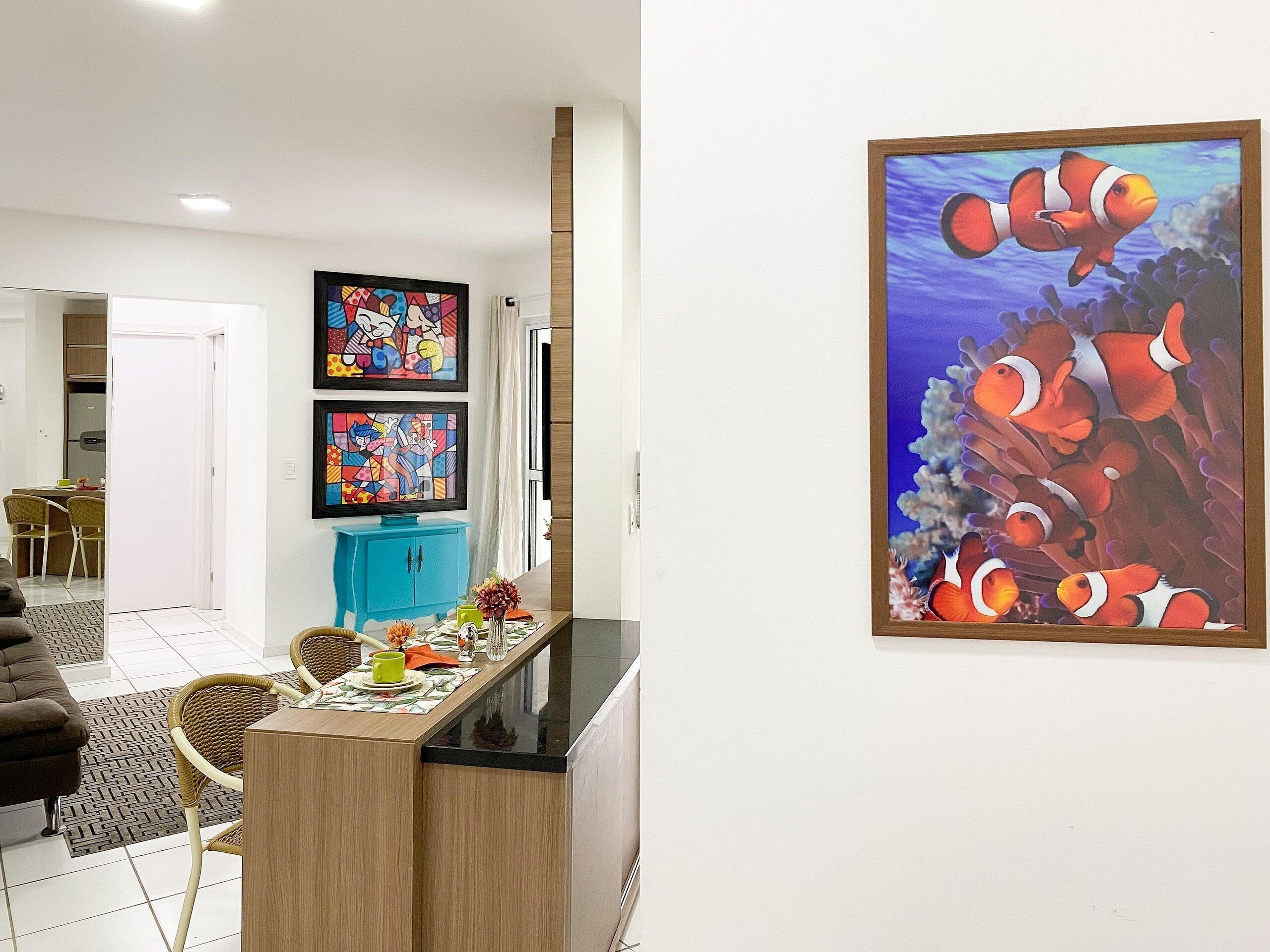 A modern kitchen with a dining area, featuring a wooden table, chairs, and a colorful painting of fish.