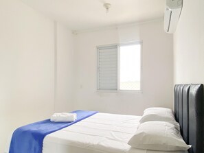 Una habitación sencilla y limpia con cama, ventana con persianas y aire acondicionado de pared.