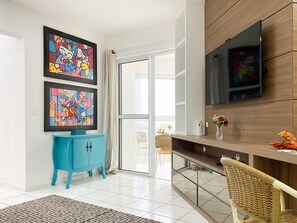 Un salon moderne avec un meuble bleu, un grand téléviseur fixé au mur et un fauteuil en osier.
