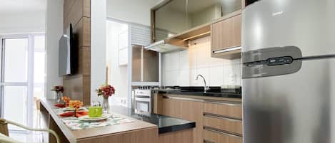 A modern kitchen with wooden cabinets, a stainless steel refrigerator, and a dining area with wicker chairs.
