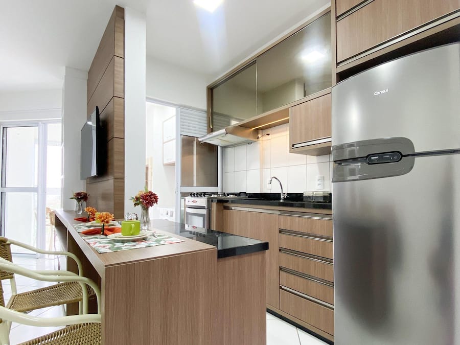 A modern kitchen with wooden cabinets, a stainless steel refrigerator, and a dining area with wicker chairs.