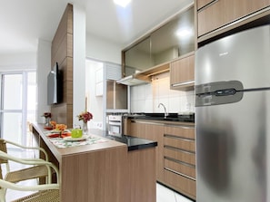 A modern kitchen with wooden cabinets, a stainless steel refrigerator, and a dining area with wicker chairs. - Resid. Clube Mar Grosso-Laguna - LAG504 (Laguna)