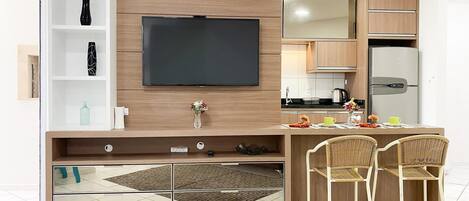 A modern kitchen with a built-in TV, wooden cabinets, and a dining area with wicker chairs.