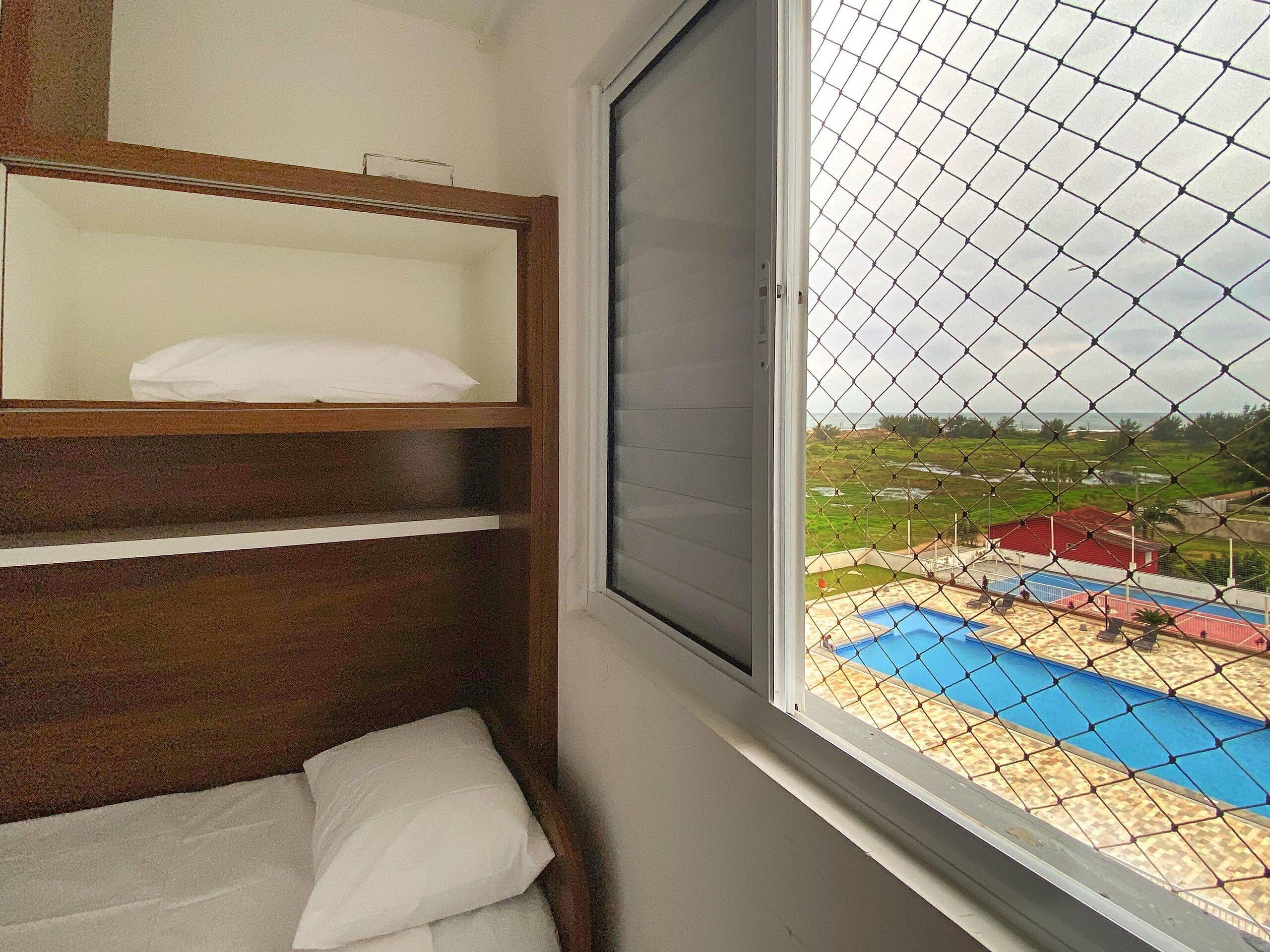A room with a window overlooking a fenced outdoor area with a pool and sports court.