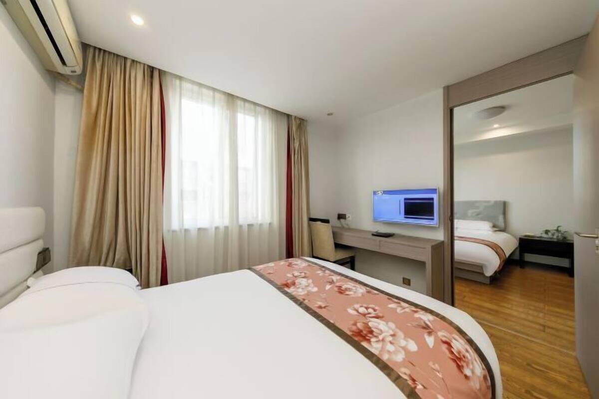 A hotel room with a bed, a desk with a computer, a TV, and a separate sleeping area with a bed.