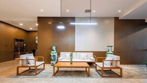 Un hall d’entrée moderne avec un comptoir d’accueil en bois, un canapé blanc et deux fauteuils en bois.