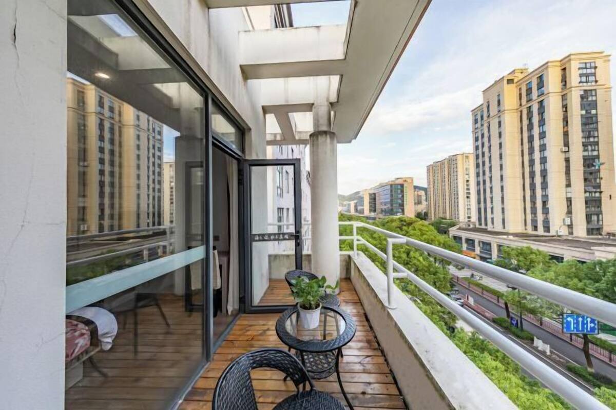 A balcony with a wooden floor, a glass door, a small table with chairs, and a potted plant.