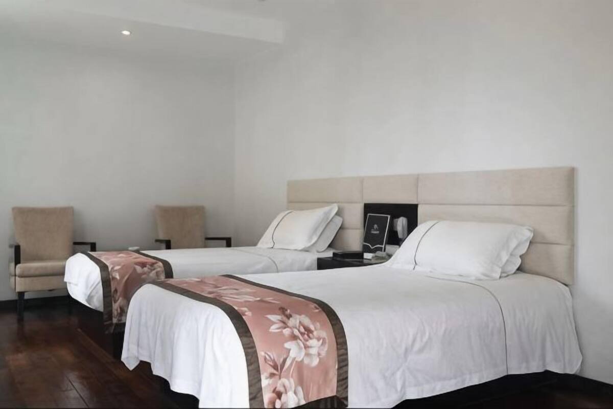 A hotel room with two beds, a chair, a bedside table, and a nightstand.