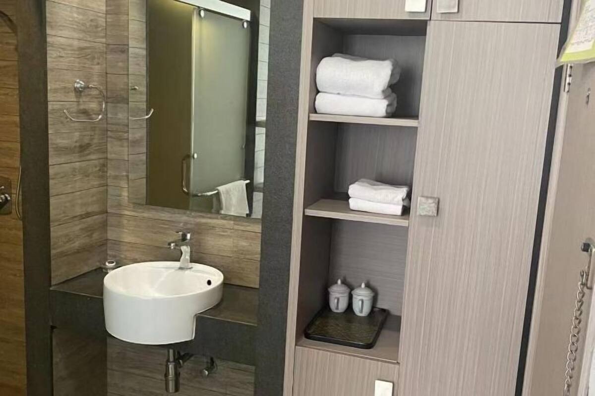 A modern bathroom with a large sink, a mirror, and a shelf with towels and toiletries.