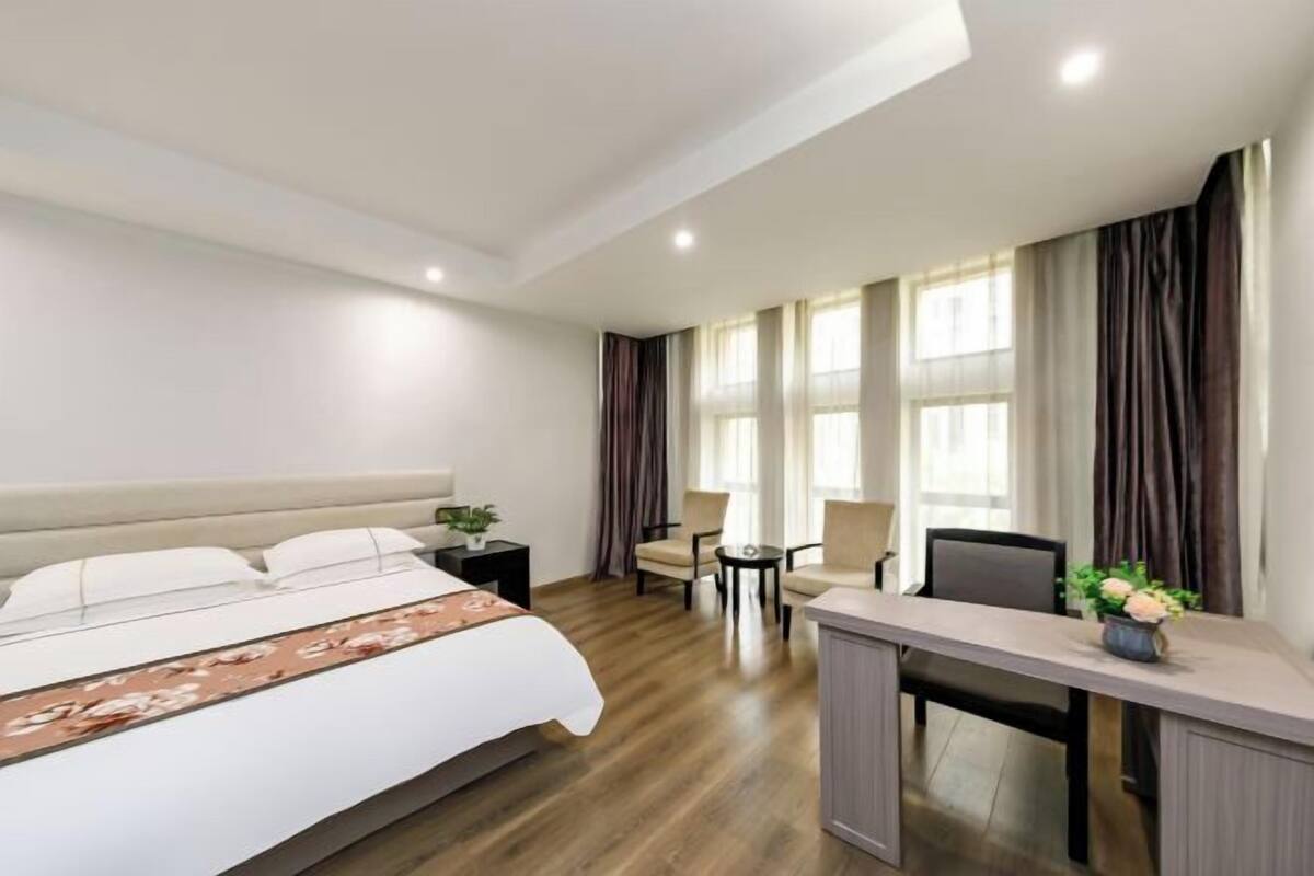 A hotel room with a bed, a desk, two chairs, a small table, and a window with curtains.