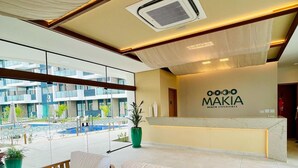 A modern hotel lobby with a reception desk, a pool view, and a seating area with wooden furniture. - Flat Makia Beach Experience - Muro Alto (Ipojuca)