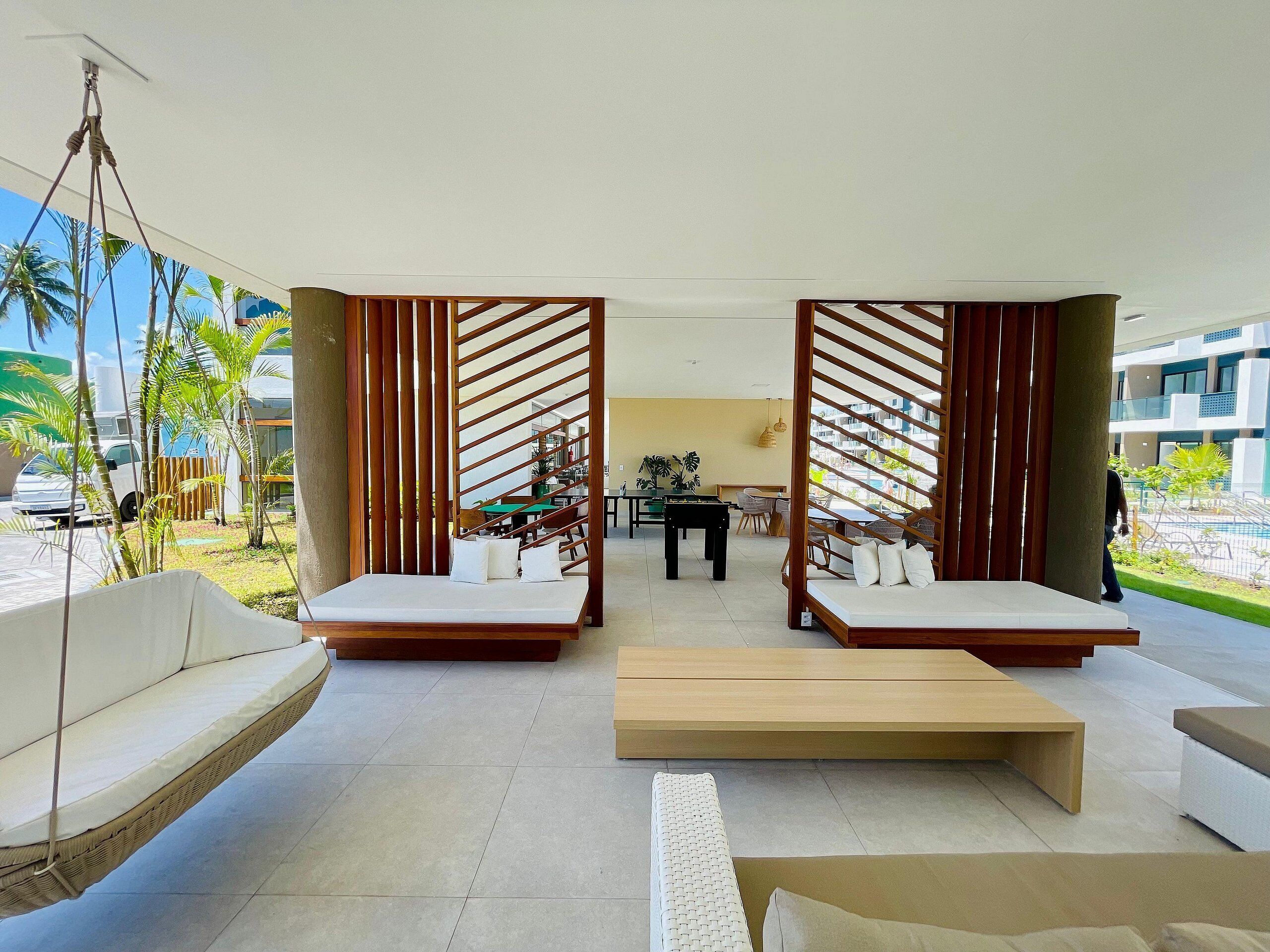 A modern lounge area with a hanging chair, two cushioned seating areas, and a wooden coffee table.