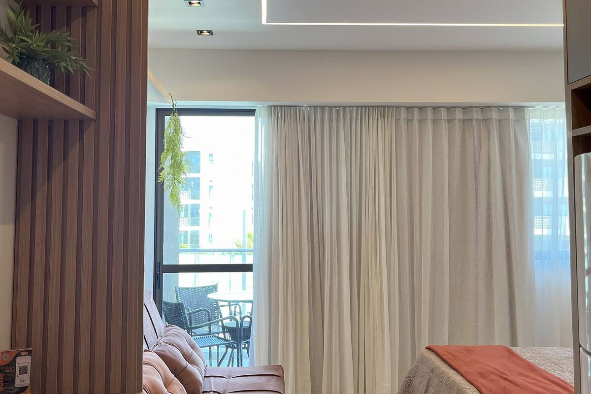 A modern bedroom with a sofa, a bed, a dining area with chairs, and a view of the outside.