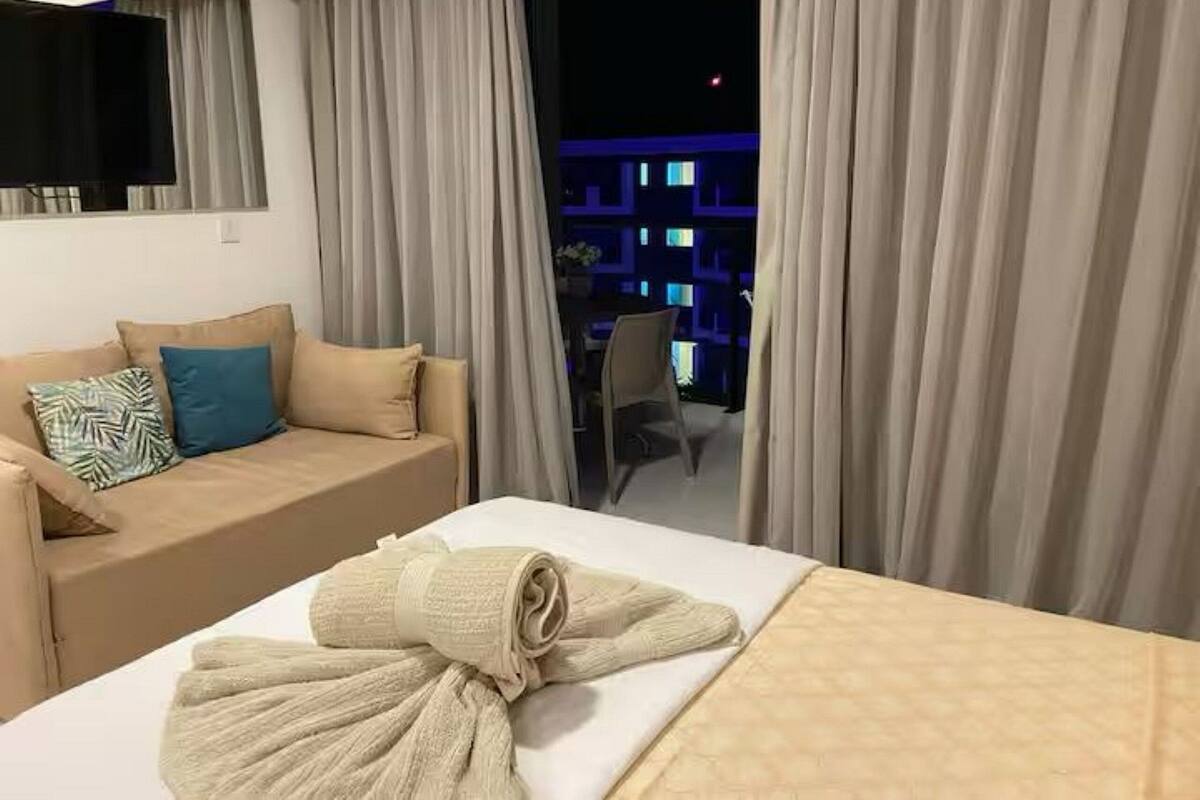 A hotel room with a bed, a sofa, a window with curtains, and a view of buildings at night.
