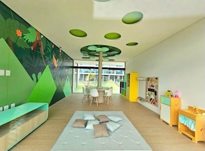 A children's play area with a mural, a seating area, and a view of the outdoors.