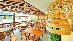A restaurant with wooden tables and chairs, a woven ceiling light fixture, and large windows allowing natural light. - Flat Makia Beach Experience - Muro Alto (Ipojuca)