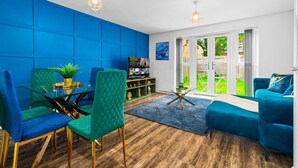 En moderne stue med blå vægge, en grøn sofa, en turkis lænestol og et spiseområde med et glasbord og stole.