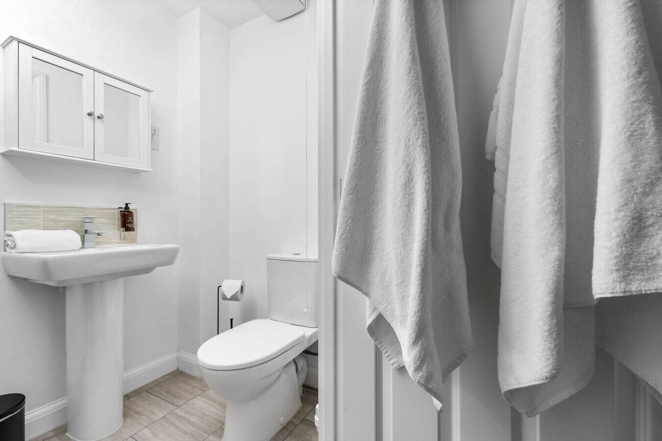 A modern bathroom with a white sink, toilet, and cabinet.