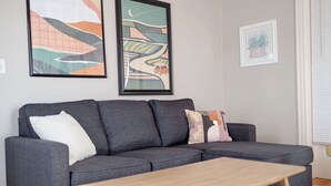 A grey sofa with three cushions, a wooden coffee table, and two framed artworks on the wall.