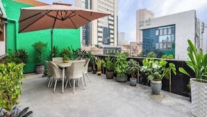 En tagterrasse med spisebord og stole, omgivet af plantekasser, under en stor parasol.