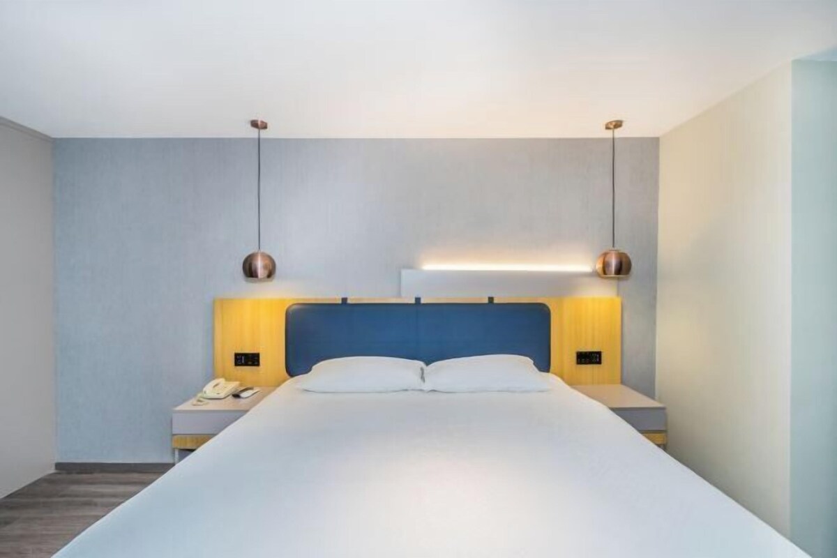 A modern hotel room with a large bed, two bedside tables with lamps, and a blue headboard.