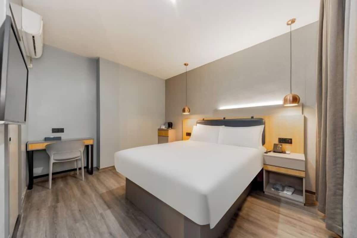 Ett modernt hotellrum med en stor säng, sängbord, ett skrivbord och en stol.
