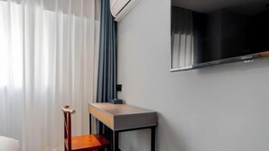 Et moderne værelse med en træstol, et lille bord, et ophængt TV og et vindue med gardiner.