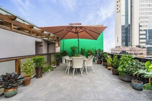 A rooftop terrace with outdoor furniture, potted plants, and a green screen backdrop.