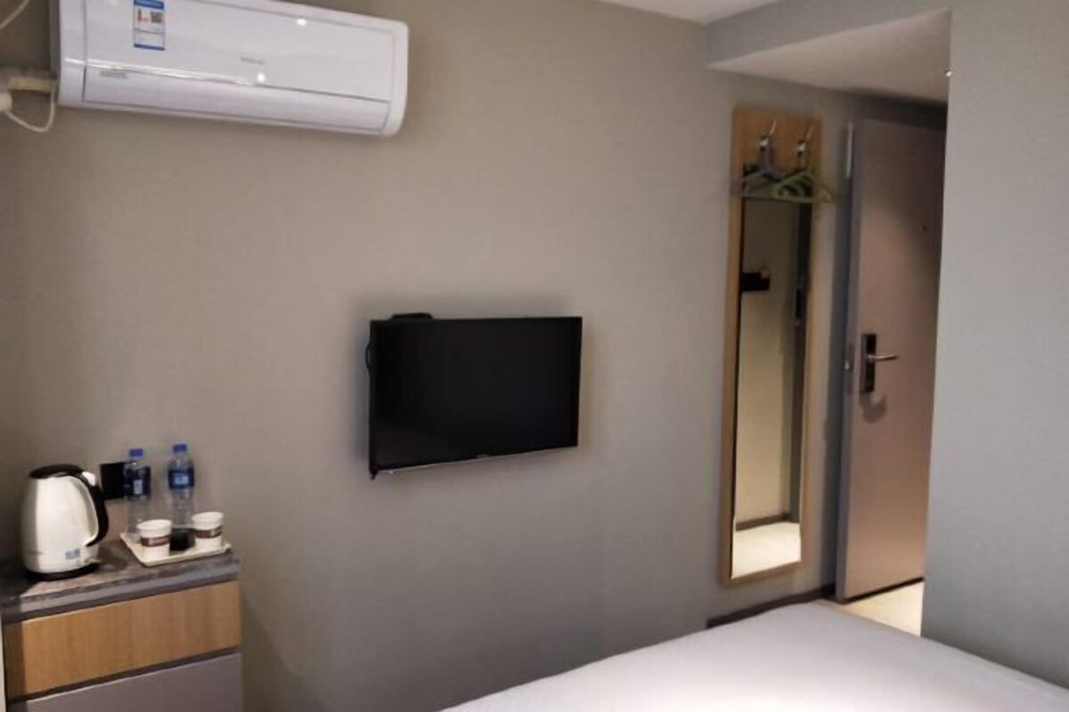A hotel room with a bed, a flat-screen TV mounted on the wall, a coffee maker, and a mirror.