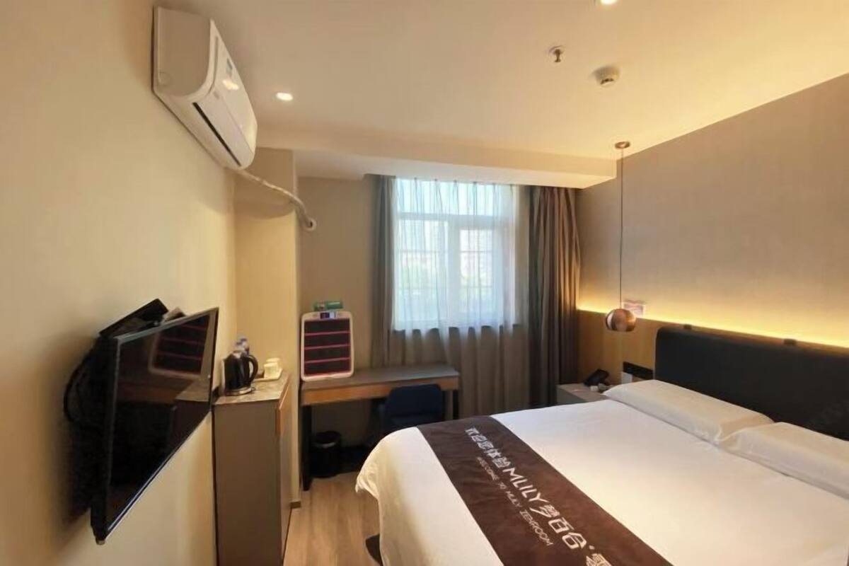 Ett hotellrum med en säng, ett skrivbord med en dator, en luftkonditioneringsanläggning och ett fönster med gardiner.