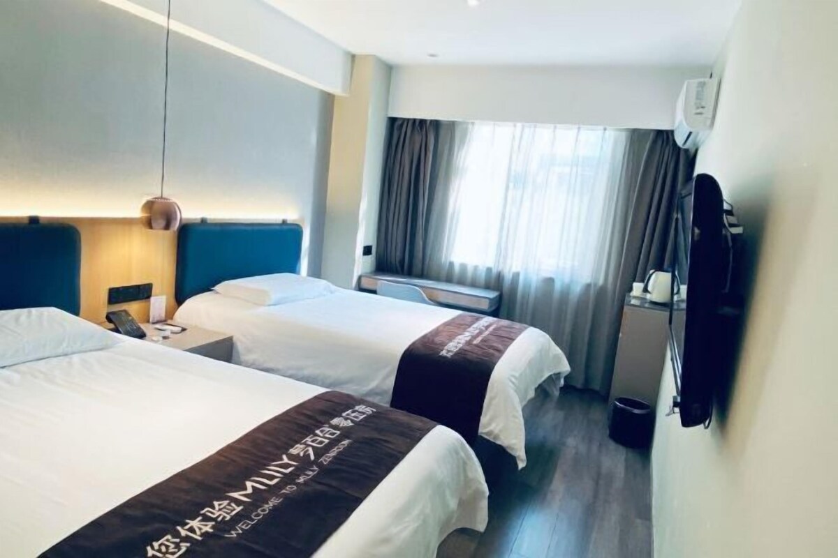 A hotel room with two beds, a desk, a chair, a TV, and a window with curtains.
