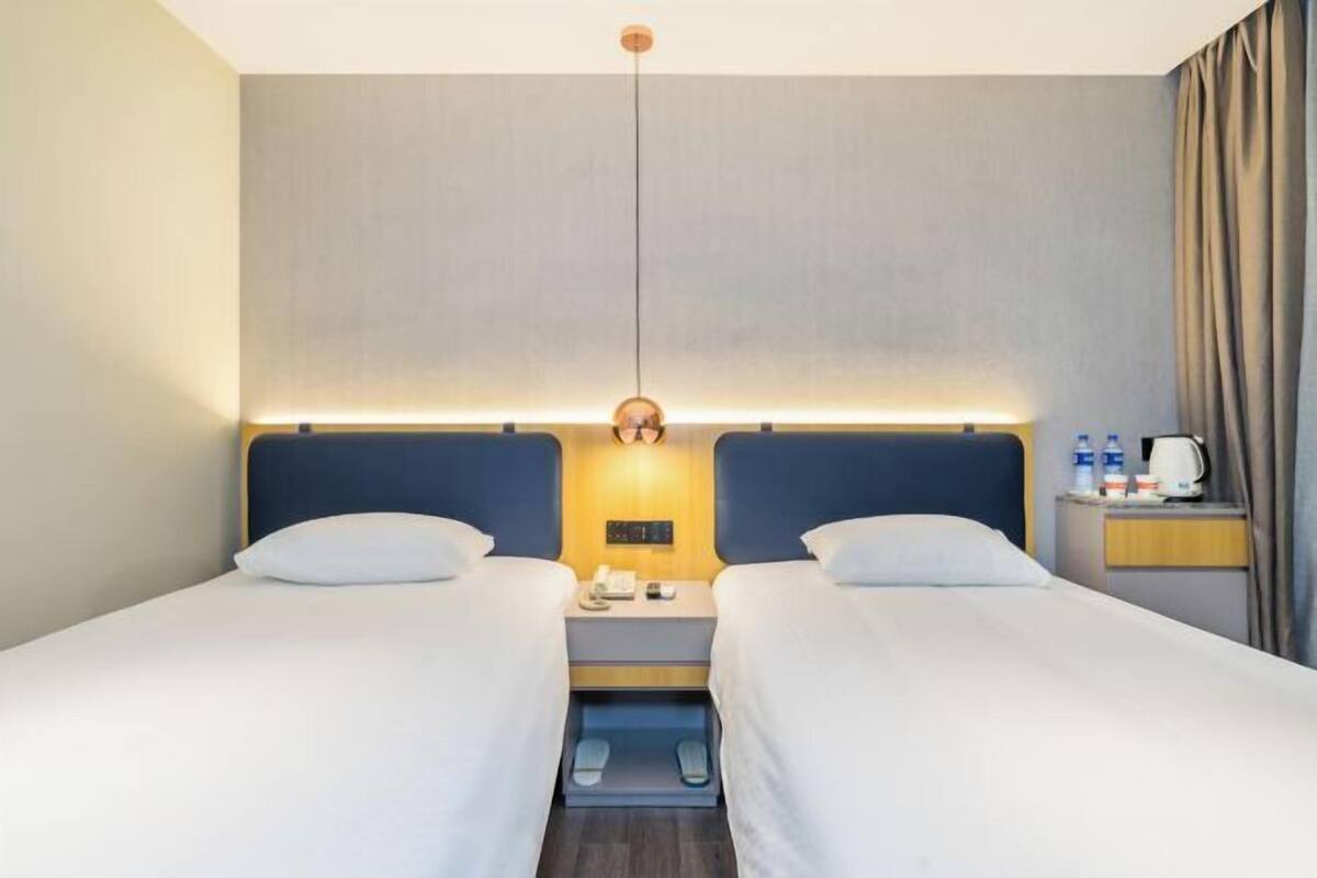 Ett hotellrum med två sängar, ett nattduksbord med en lampa, ett litet bord med en vattenkokare och en gardin vid fönstret.