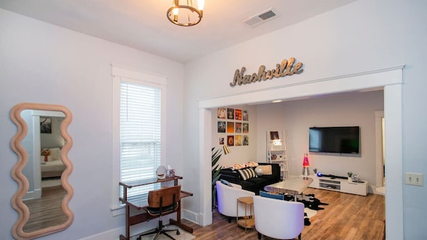 A modern living room with a large mirror, a black sofa, a white armchair, and a TV mounted on the wall. - Neon Nashville! 5 min to Broadway •Walk 2 dining! (Nashville)