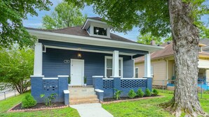 A single-story house with a dark blue exterior, a front porch with a white door, and a small front yard with a tree and a sidewalk. - Neon Nashville! 5 min to Broadway •Walk 2 dining! (Nashville)