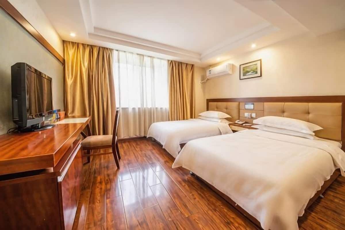 Ein Hotelzimmer mit zwei Betten, einem Schreibtisch mit Fernseher und einem Fenster mit Vorhängen.
