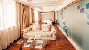A hotel room with a sofa, a glass coffee table, a bed, and a wall with a geometric pattern. - Shui Yun Jian Xinghualou Hotel (Chizhou)
