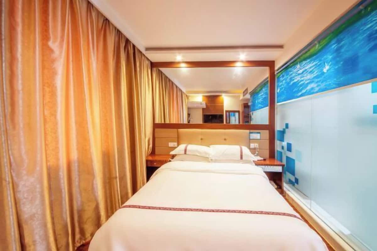 Ein Hotelzimmer mit einem Bett, Vorhängen, einem Kopfteil, einem Nachttisch, einem Spiegel und einer Wand mit einem blauen Kunstwerk.