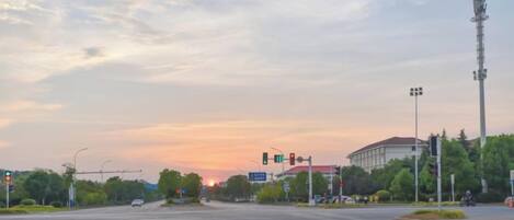 A wide intersection with traffic lights, a clear sky, and distant buildings.