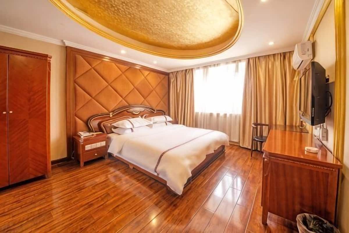 Ein Hotelzimmer mit einem großen Bett, Holzboden, einem Kleiderschrank, einem Schreibtisch und einem Fernseher.