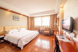 Een hotelkamer met een groot bed, een bureau met stoel, een televisie en een raam met gordijnen.