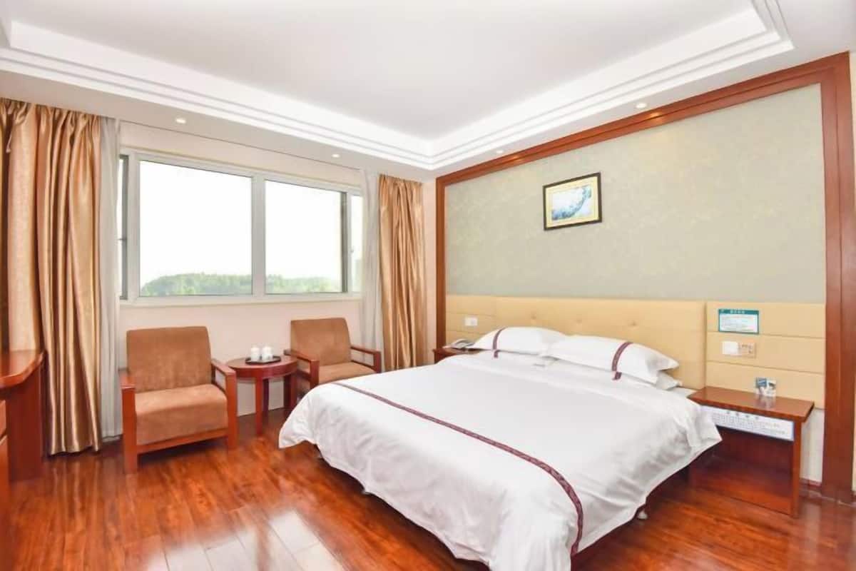 Ein Hotelzimmer mit einem großen Bett, einem Schreibtisch, einem Sessel, einem Fenster und einem Bild an der Wand.