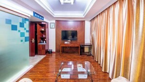 A hotel room with a wooden floor, a glass coffee table, a flat-screen TV mounted on the wall, and a curtain on the right side. - Shui Yun Jian Xinghualou Hotel (Chizhou)