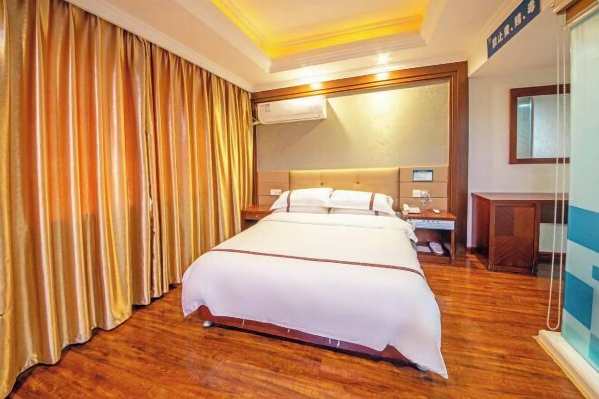 Ein Hotelzimmer mit einem großen Bett, einem Nachttisch, einem Schreibtisch und einer Klimaanlage.