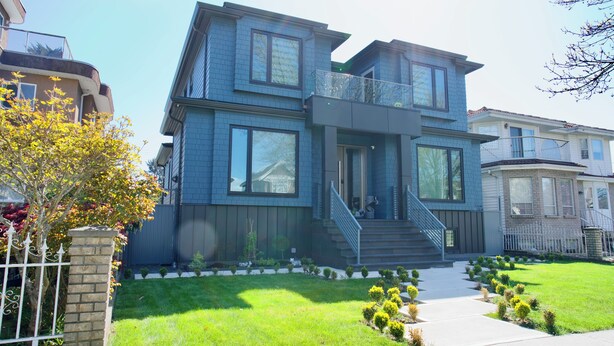 A modern two-story house with a balcony, a front yard with a pathway, and a small garden.