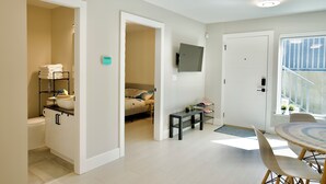 A modern, well-lit room with a bed, bedside table, and a small seating area with a table and chairs.