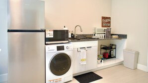 A compact kitchen with a stainless steel refrigerator, microwave, and washing machine, a sink, and a coffee maker.